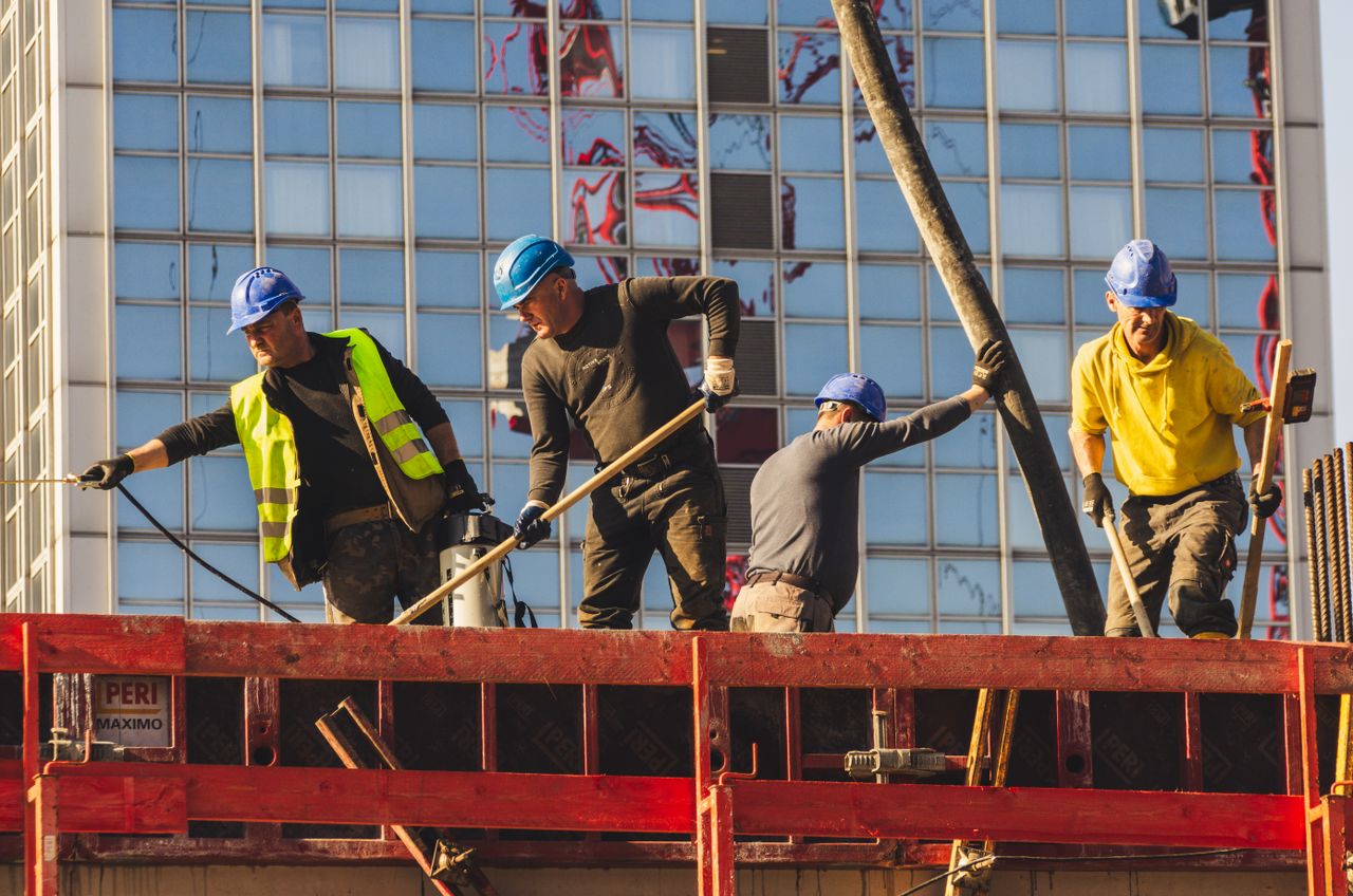 Home A group of construction workers in safety gear actively working on a high-rise building site.